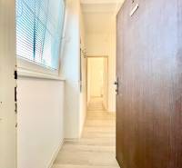 Ein Flur mit einem Boden in Holzoptik, weißen Wänden, einem großen Fenster mit Jalousien.