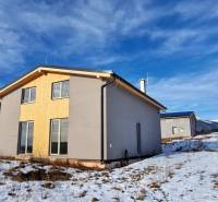 Eine Hütte in Dolná Lehota mit Holzverkleidung, verschneite Landschaft und Berge am Horizont.