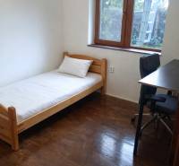 Einfaches Zimmer mit Bett, Tisch und Boden in Holzoptik in einer 3-Zimmer-Wohnung.
