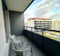 Ein Balkon mit zwei Stühlen und Fliesen in Holzoptik, Blick auf Gebäude.