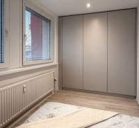 Schlafzimmer einer 2-Zimmer-Wohnung mit Einbauschrank, großem Fenster und Boden in Holzoptik.