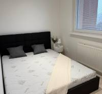 Schlafzimmer in einer 2-Zimmer-Wohnung mit schwarzem Kopfteil, weißer Bettdecke und Fenster mit Rollläden.