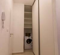 Ein enger Flur in einer Einzimmerwohnung mit einer Waschmaschine und Schiebetüren.