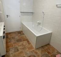 Das Badezimmer im Einfamilienhaus hat eine Badewanne, weiße Fliesen und einen Boden mit Holzdekor.