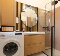 Badezimmer mit Waschmaschine, Waschbecken, Spiegel und Duschkabine in einer 3-Zimmer-Wohnung.