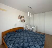Schlafzimmer in einer 3-Zimmer-Wohnung mit einem Doppelbett, einem Kinderbett und einem Boden mit Holzdekor.