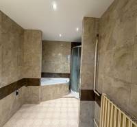 Ein Badezimmer in einem Einfamilienhaus mit Marmoroptikfliesen und einer Eckbadewanne.