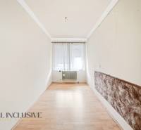 Ein schmaler Raum mit einem Holzboden, einem Fenster mit Vorhängen und einem Heizkörper.