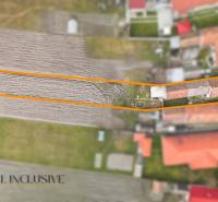 Ein Einfamilienhaus in Topoľníky mit Garten im Rahmen, sichtbar sind landwirtschaftliche Felder und Gebäude.