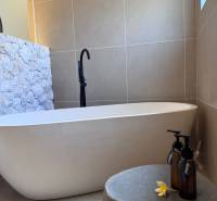 Ein Badezimmer in einem Einfamilienhaus mit einer Badewanne, einer mit Stein verkleideten Wand und dekorativen Fläschchen.