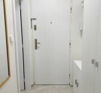 Eingangstür in einem Einzimmerapartment mit weißen Wänden und Fliesen, Spiegel an der Wand.