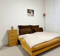 Einzimmerwohnung mit Bett, Nachttisch und Teppich, zarte Vorhänge am Fenster.