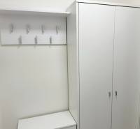 Ein heller Schrank und ein Kleiderständer in einem Studio mit mehreren Haken und einem weißen Tisch.