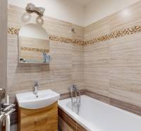 Badezimmer in einer 2-Zimmer-Wohnung mit hellen Fliesen und Badewanne, Schränke unter dem Waschbecken.