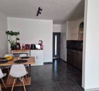 Küche in einer 3-Zimmer-Wohnung mit Esstisch, dunklem Boden und weißen Stühlen.