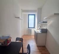 Ein schmales Büro mit einem schwarzen Tisch, Stühlen und einem Boden in Holzoptik.