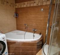 Badezimmer in einer 3-Zimmer-Wohnung mit Eckbadewanne und Waschmaschine, Fliesen mit Bambusmuster.