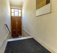 Eine enge Treppe mit einer Leiter und einer Lampe führt zu einer Holztür. Büros.