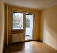 Ein leerer Raum in einer 3-Zimmer-Wohnung mit Holzdekorboden und verglasten Balkontüren.