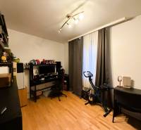 Ein Zimmer mit einem Holzboden, einem Schreibtisch, einem Computer, einem Heimtrainer, Regalen.