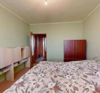 Schlafzimmer in einer 4-Zimmer-Wohnung mit einer hellen Wand und einem Bett mit Blumenmuster.