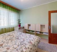 Schlafzimmer in einer 4-Zimmer-Wohnung mit grünen Vorhängen und gemusterter Bettwäsche.