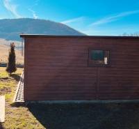 Kleines Holzhaus auf der Straße in Prosačov mit Blick auf die Hügel und blauen Himmel.