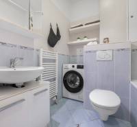 Badezimmer in einer Einzimmerwohnung mit Waschmaschine, Waschbecken und Badewanne, hellblaue Fliesen.