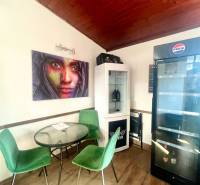 Gastronomische Räume mit Holzboden, grünen Stühlen, Bildern und Kühlschrank.