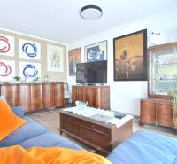 Wohnzimmer in einer 3-Zimmer-Wohnung mit Holzmöbeln, Boden mit Holzdekor und Bildern an den Wänden.