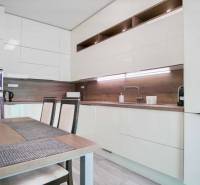 Küche in einer 3-Zimmer-Wohnung mit glänzenden Schränken und Holzwanddekoration.