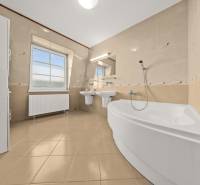 Ein Badezimmer in einem Einfamilienhaus mit Badewanne, Waschbecken, Fenster und hellen Fliesen.