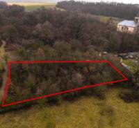 Erholungsgrundstücke in Gemerské Teplice, umgeben von Bäumen, mit einem historischen Kirchengebäude im Hintergrund.