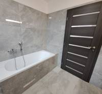 Ein Badezimmer in einem Einfamilienhaus mit einer Badewanne, grauen Fliesen und dunklen Türen.