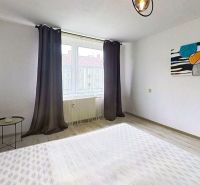 Ein helles Zimmer mit einem Bett, dekorativer Malerei und einem Boden mit Holzdekor in einer 3-Zimmer-Wohnung.