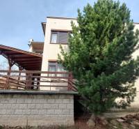 Ein Einfamilienhaus in Zlaté Moravce mit einer Holzterrasse, einem hohen Baum und einem Garten.