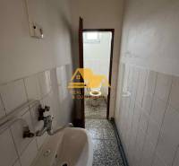 Einzimmerwohnung mit engem Badezimmer mit Waschbecken und Toilette, gefliest mit weißen Fliesen.
