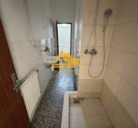 Badezimmer in einem Studio-Apartment mit einer einfachen Duschkabine, einem Waschbecken und Fliesen.