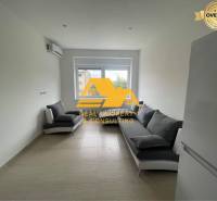 Wohnzimmer in einer 3-Zimmer-Wohnung mit zwei grauen Sofas und einem weißen Kühlschrank.