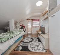 Ein Dachbodenzimmer in einem Einfamilienhaus mit Bett, Fernseher, Dekorationen und einem Boden in Holzoptik.