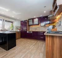 Eine Küche in einem Einfamilienhaus mit glänzenden violetten Schränken und einem Boden in Holzoptik.