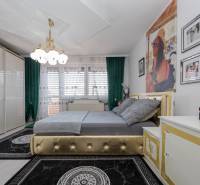 Schlafzimmer im Einfamilienhaus mit Bett, grünen Vorhängen und goldenen Details an den Möbeln.