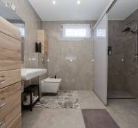 Badezimmer eines Einfamilienhauses mit Fliesen und Duschkabine, Schränke mit Holzdekor.