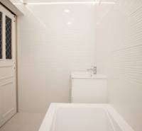 Badezimmer in einer 2-Zimmer-Wohnung mit weißen Fliesen, Waschbecken und Badewanne.