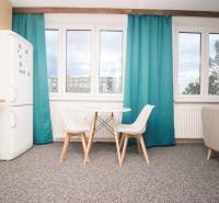 Küche mit Tisch und Stühlen in einer 4-Zimmer-Wohnung, Schrank und Fenster mit türkisfarbenen Vorhängen.