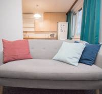 Ein graues Sofa mit bunten Kissen in einer Vierzimmerwohnung am Fenster und in der Nähe der Küche.