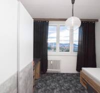 Ein Zimmer in einer 4-Zimmer-Wohnung mit einem Bett, dunklen Vorhängen und einem Blick aus dem Fenster.