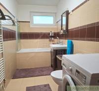 Badezimmer im Einfamilienhaus mit Badewanne, Waschmaschine und braun-beigen Fliesen.