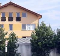 Das gelbe Haus mit dem schrägen Dach und den Fenstern hinter den Bäumen in der Nähe der Bürogebäude.