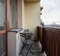 Ein Balkon mit einem hölzernen Geländer und einem Tisch mit zwei Stühlen in einer Wohnung mit fünf oder mehr Zimmern.